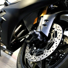 Black front axle sliders for motorcycle body protection, branded by SHOGUN, shown mounted on a motorcycle frame.