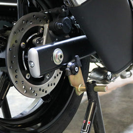 Black SHOGUN swingarm sliders for motorcycle body protection, shown installed on a bike's swingarm in a close-up shot.