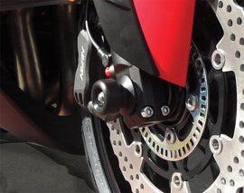 Black front axle sliders for motorcycle body protection, designed by SHOGUN, shown attached to a motorcycle's front axle.