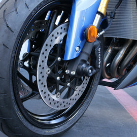 Black front axle sliders for body protection, branded by SHOGUN, shown mounted on a motorcycle.